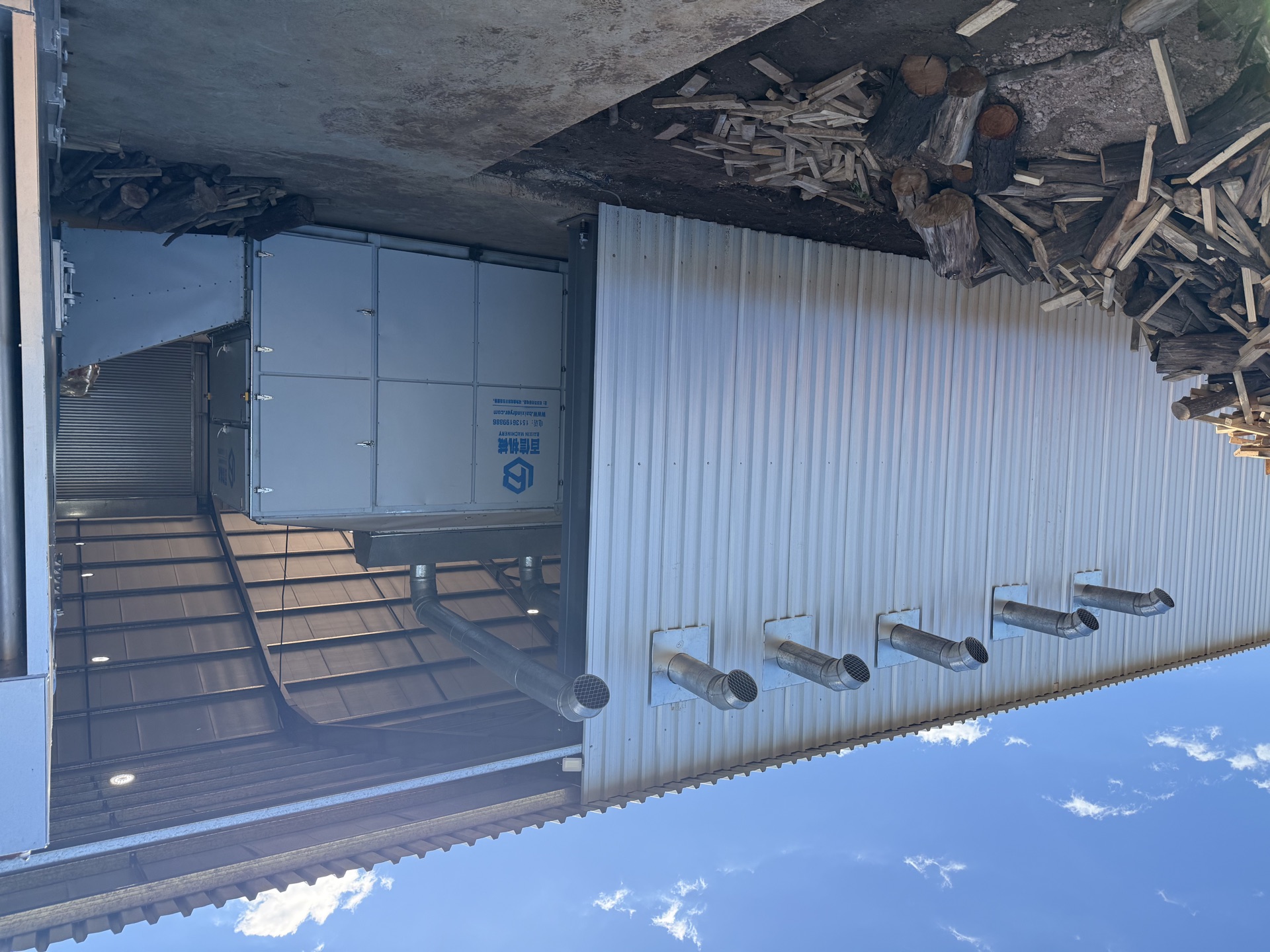 Exterior of the Wostevia processing facility showing extractor flues and stacked firewood